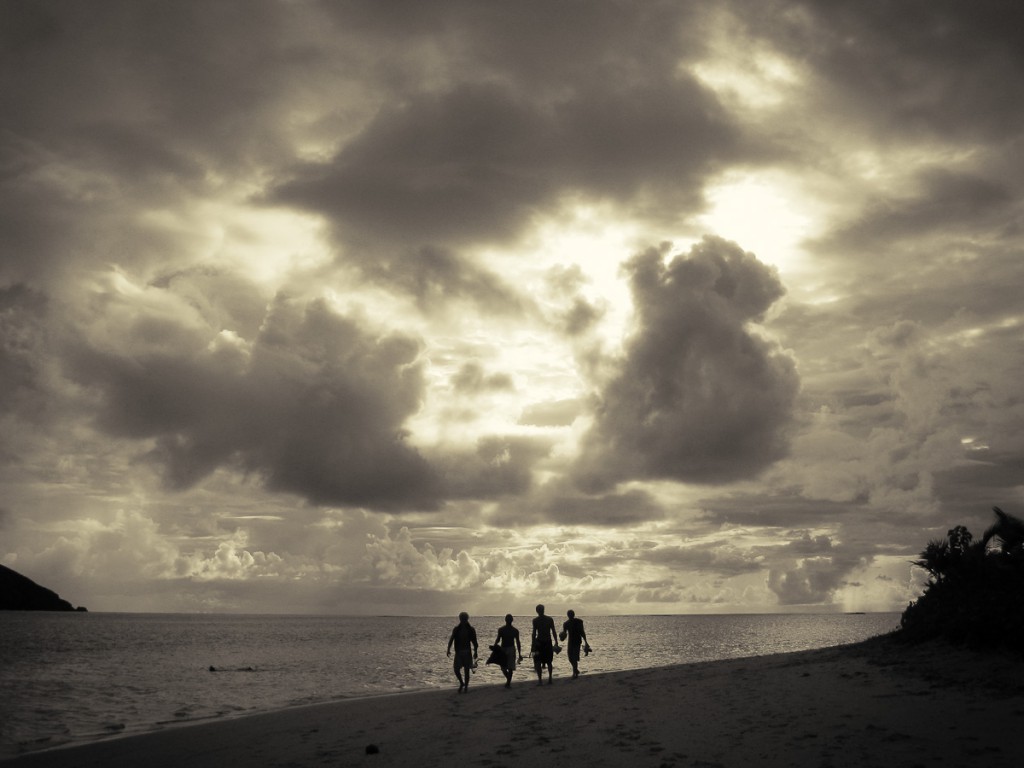 dramatic clouds behind surfers walking on the beach in Fiji