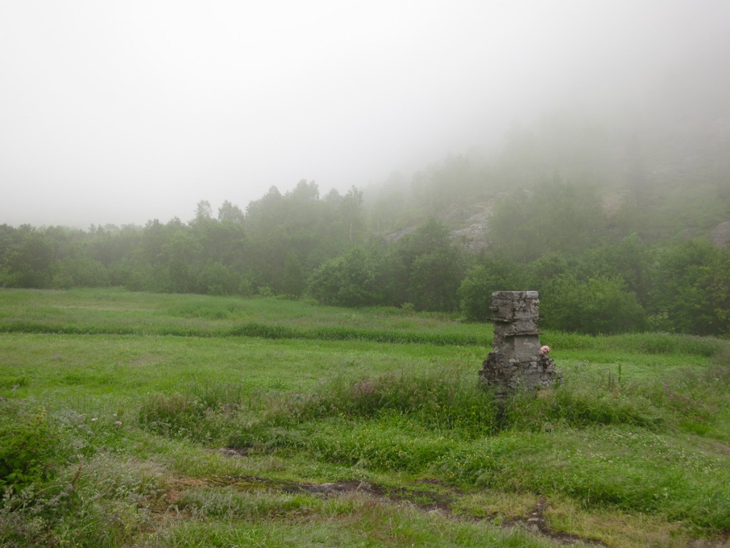 man hiding behind old chimney in foggy green field